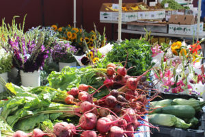 Farmers market booth with fresh herbs, vegetables, and cut flowers